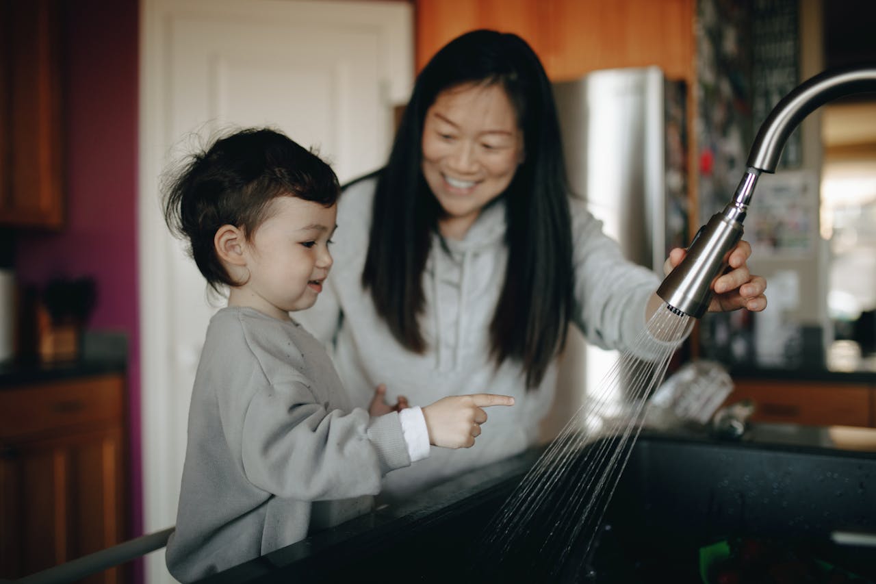 services-03 A mother and child happily wash hands together at a kitchen sink, sharing a bonding moment indoors.